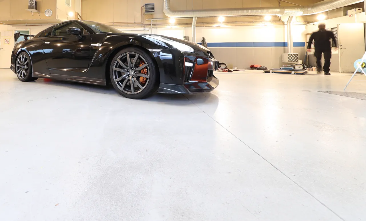 Sergio går gennem det lyse værksted forbi en sort Nissan GT-R
