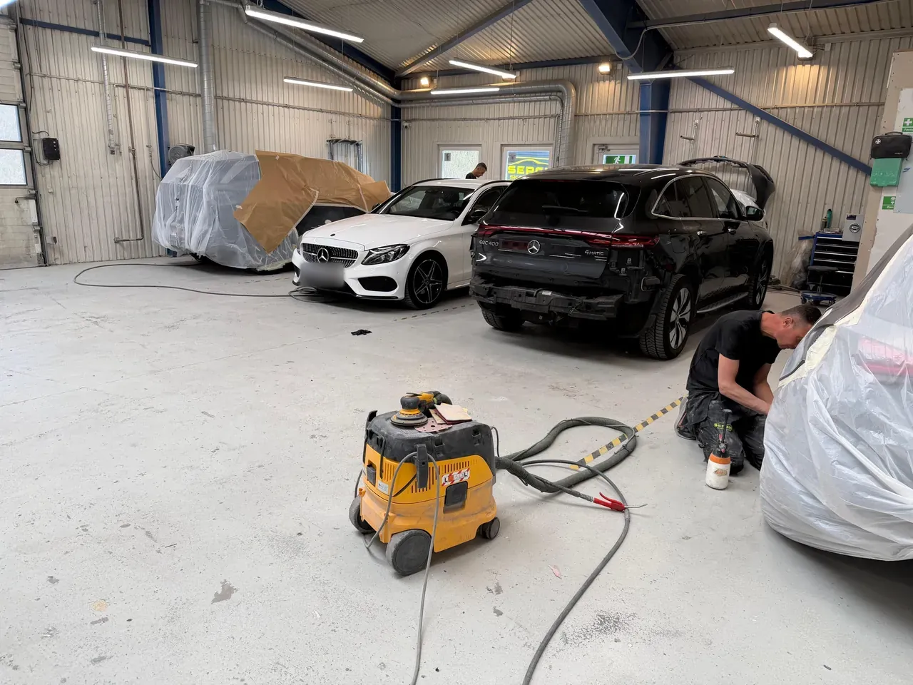 Værkstedsgulvet med støvsuger og biler under arbejde