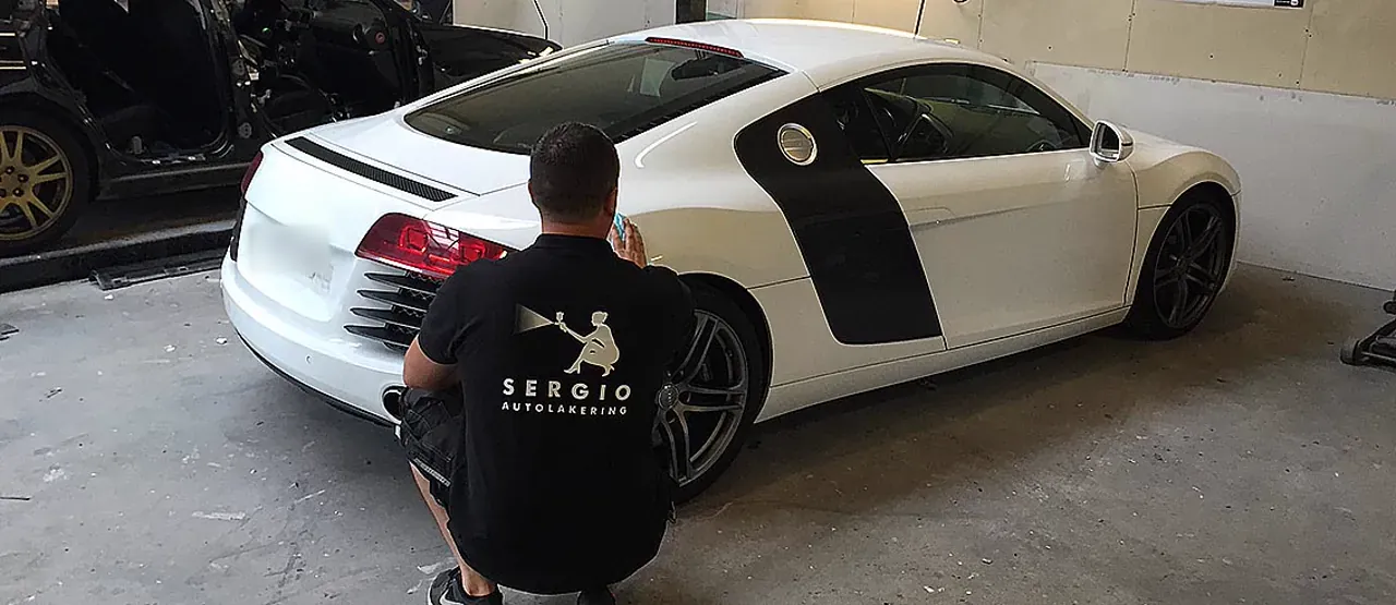 Sergio i hug ved en hvid Audi R8 med sorte striber inde i værkstedet
